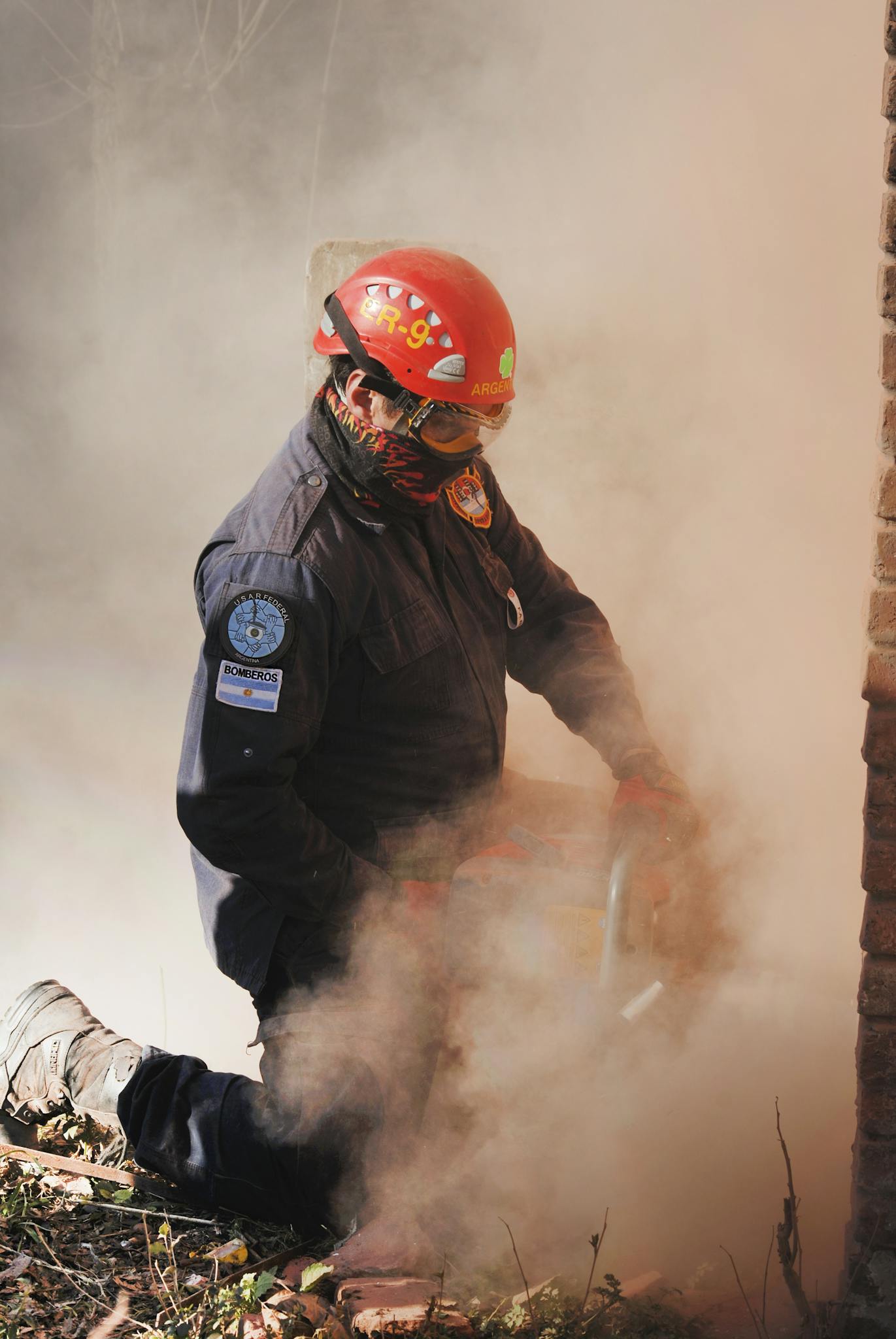 A firefighter wearing safety gear operates a chainsaw amidst dense smoke during a training exercise, showcasing emergency readiness.
